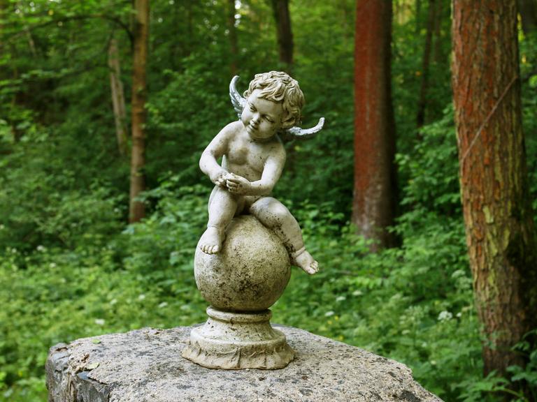 Ein kleiner sitzender Engel auf einem Friedhof.