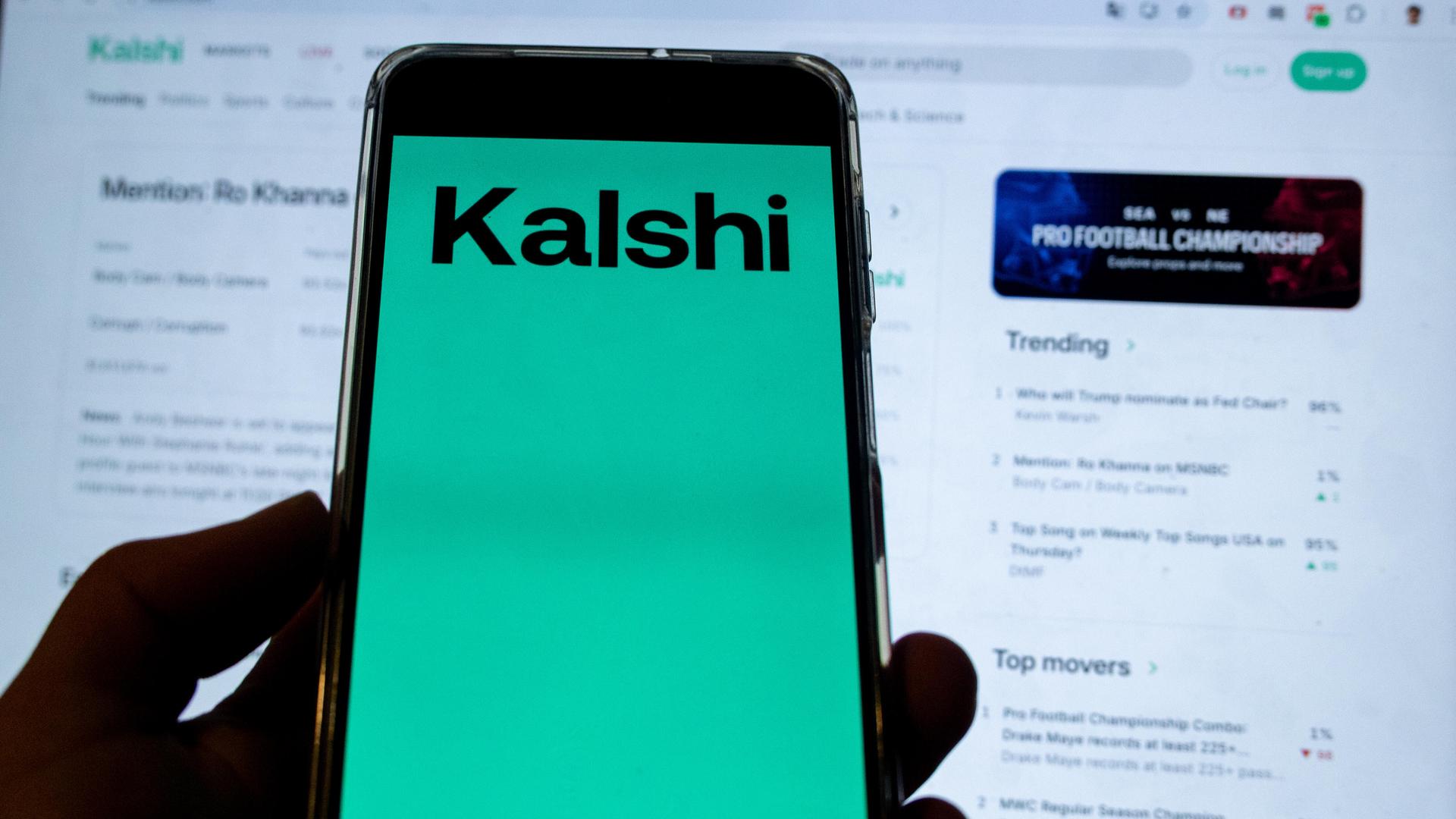 Kalshi Logo auf einem Smartphone vor einer Trading Webseite von Kalshi