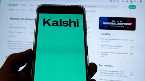 Kalshi Logo auf einem Smartphone vor einer Trading Webseite von Kalshi