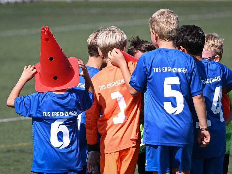 Eine Gruppe von Kindern vom TuS Erzgebirge stehen auf einem Spielfeld. Sie tragen blaue und orange Trikots und sind von hinten zu sehen. 