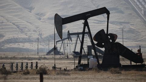 Mehrere Ölbohrtürme stehen in einer trockenen Gegend in den USA. Die metallenen Pumpanlagen mit ihren markanten Hebelarmen fördern Öl aus dem Boden.