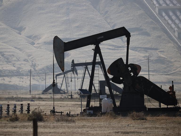 Mehrere Ölbohrtürme stehen in einer trockenen in den USA. Die metallenen Pumpanlagen mit ihren markanten Hebelarmen fördern Öl aus dem Boden.