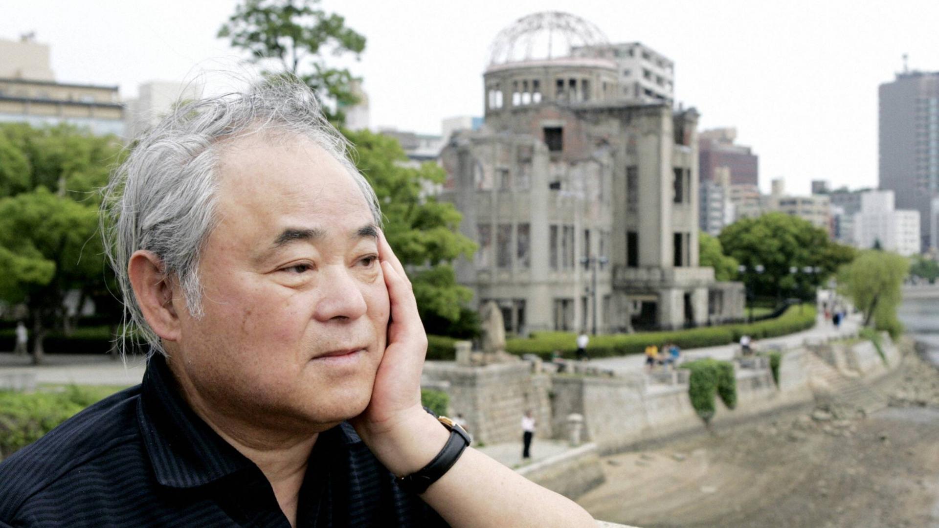 Keiji Nakazawa steht auf einer Brücke und blickt nachdenklich. Hinter ihm ist eine Ruine zu erkennen. Das Gebäude wurde beim Atombombenabwurf über Hiroshima am 6. August 1945 zerstört.