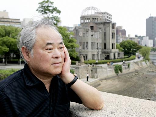 Keiji Nakazawa steht auf einer Brücke und blickt nachdenklich. Hinter ihm ist eine Ruine zu erkennen. Das Gebäude wurde beim Atombombenabwurf über Hiroshima am 6. August 1945 zerstört.