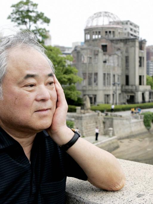 Keiji Nakazawa steht auf einer Brücke und blickt nachdenklich. Hinter ihm ist eine Ruine zu erkennen. Das Gebäude wurde beim Atombombenabwurf über Hiroshima am 6. August 1945 zerstört.