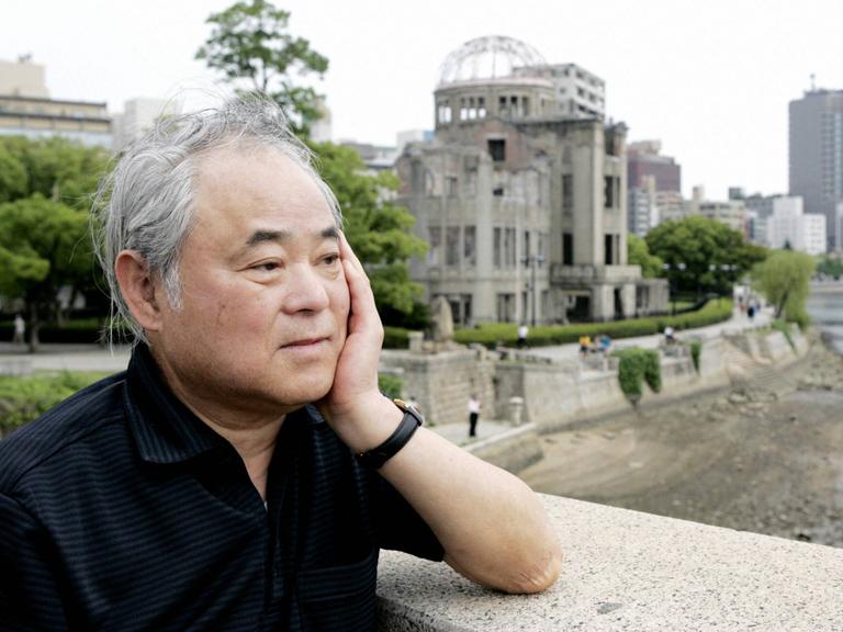 Keiji Nakazawa steht auf einer Brücke und blickt nachdenklich. Hinter ihm ist eine Ruine zu erkennen. Das Gebäude wurde beim Atombombenabwurf über Hiroshima am 6. August 1945 zerstört.