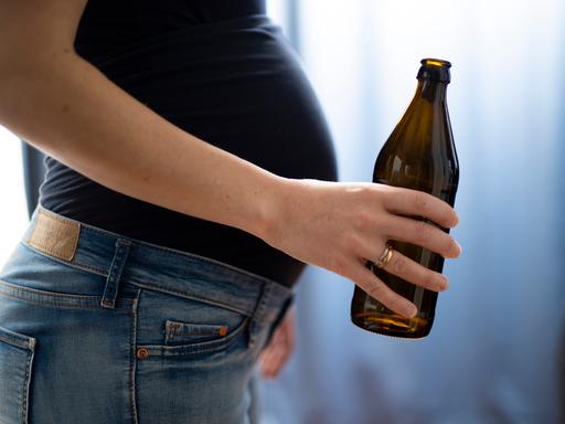 Seilticher Blick auf den Bauch einer schwangeren Frau, die eine Flasche Bier in der Hand hält