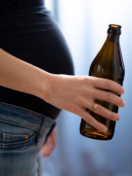Seilticher Blick auf den Bauch einer schwangeren Frau, die eine Flasche Bier in der Hand hält