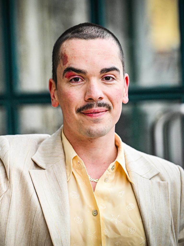 Ole Liebl steht an eine Wand gelehnt und schaut freundlich in die Kamera. Er trägt ein gelbes Hemd und helles Sakko.