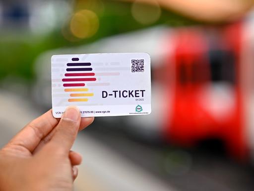 Eine Person hält ein sogenanntes Deutschlandticket für 49 Euro in der Hand. Im Hintergrund ist eine Bahnwaggon zu erkennen.