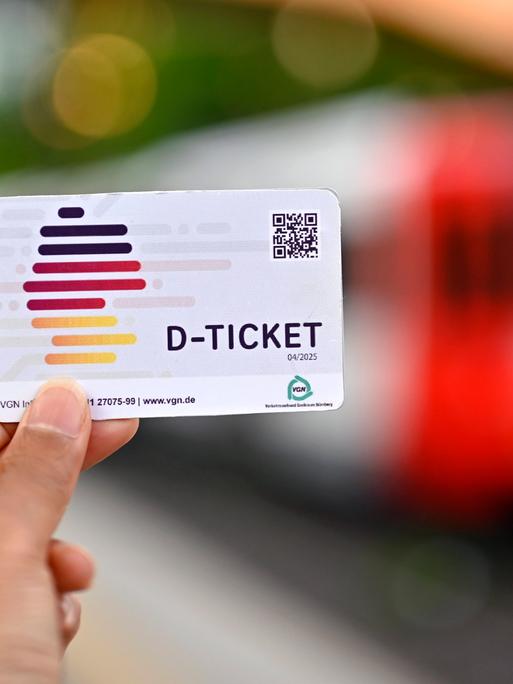 Eine Person hält ein sogenanntes Deutschlandticket für 49 Euro in der Hand. Im Hintergrund ist eine Bahnwaggon zu erkennen.