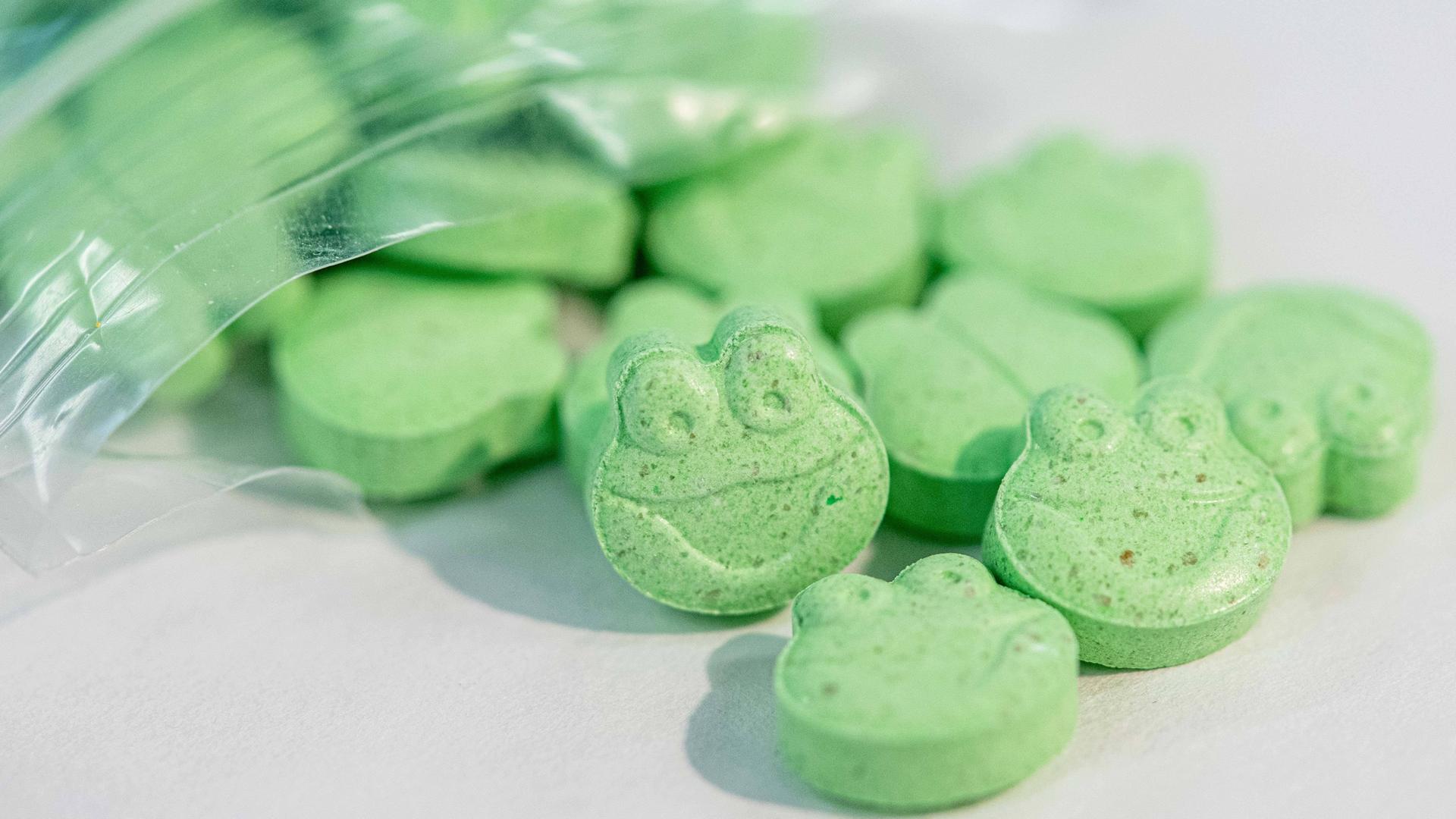 Grüne Ecstasy-Tabletten in Form eines Fischkopfes quellen aus einer kleinen Plastiktüte.