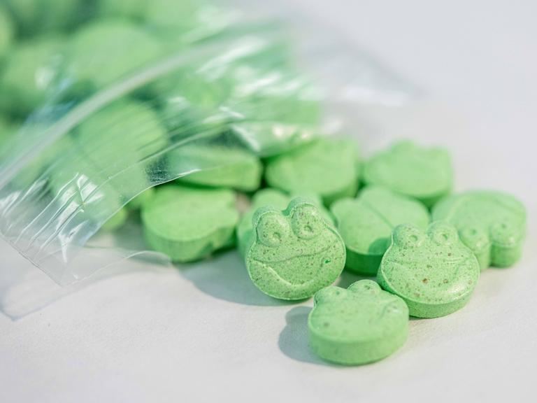 Grüne Ecstasy-Tabletten in Form eines Fischkopfes quellen aus einer kleinen Plastiktüte.