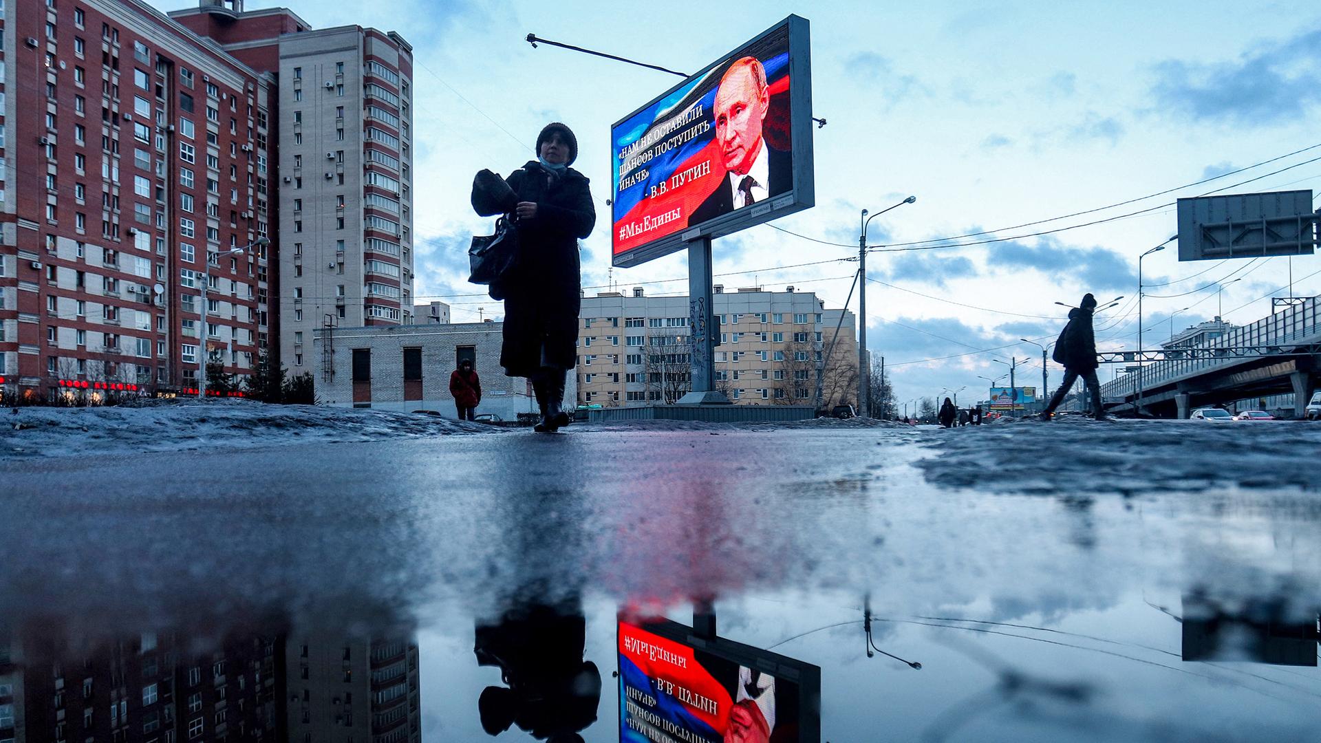 Fußgänger gehen an einer Werbetafel vorbei, auf der ein Bild des russischen Präsidenten Wladimir Putin und ein Zitat aus seiner jüngsten Rede an die Nation abgebildet sind: "Wir hatten keine andere Chance, als anders zu handeln".