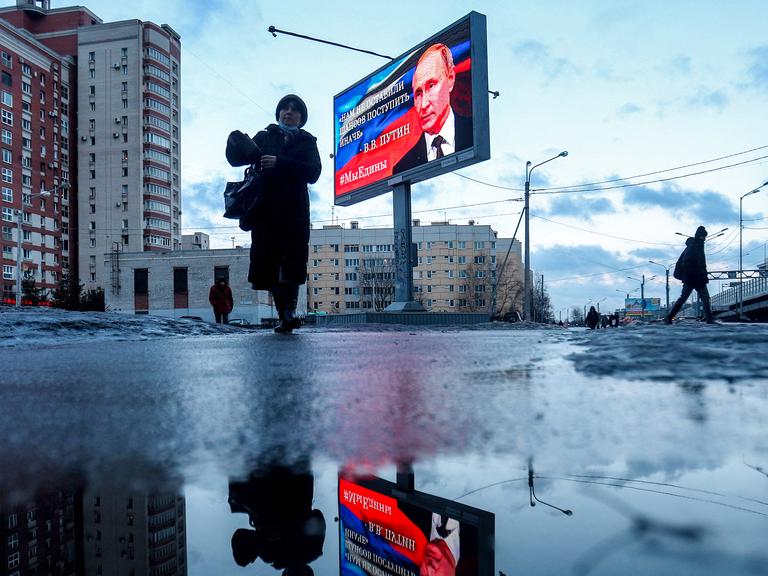 Fußgänger gehen an einer Werbetafel vorbei, auf der ein Bild des russischen Präsidenten Wladimir Putin und ein Zitat aus seiner jüngsten Rede an die Nation abgebildet sind: "Wir hatten keine andere Chance, als anders zu handeln".