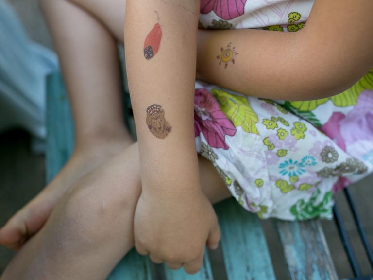 Ein kleines Mädchen trägt Klebetattoos am Arm.
