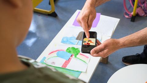 Ein Schüler wird mit dem Smartphone unterrichtet. Ein Erwachsener hält das Gerät in der Hand und zeigt dem Kind das Bild.