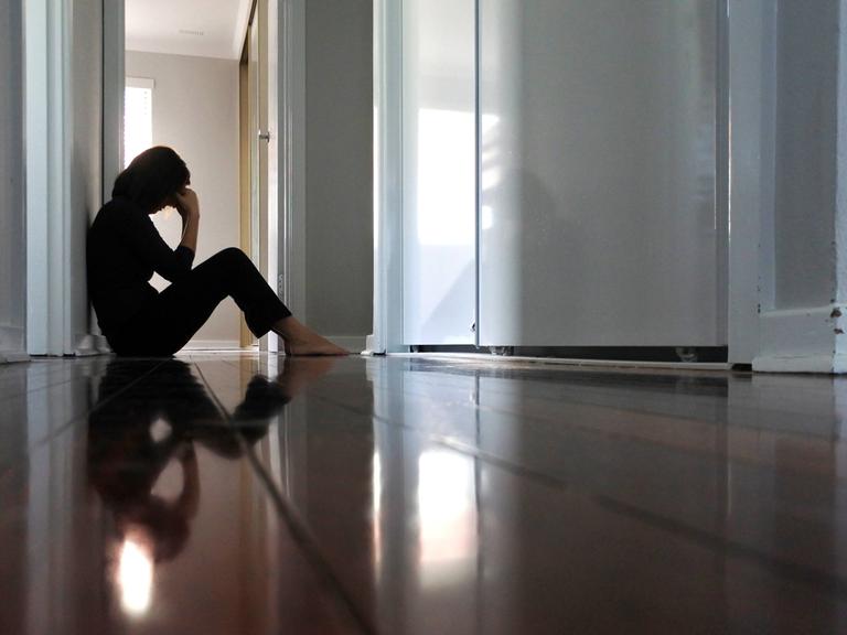 Eine junge Frau sitzt traurig im dunklen Flur