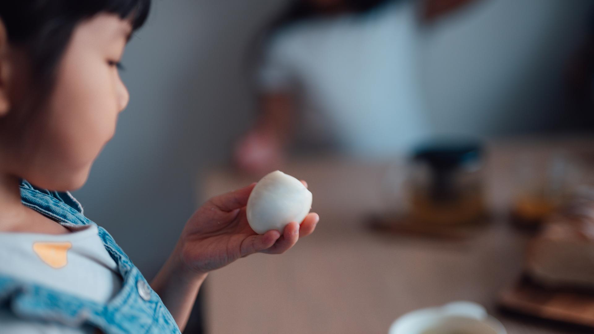 Blick über die Schulter eines Kindes, das ein angebissenes gekochtes Ei in der Hand anschaut.