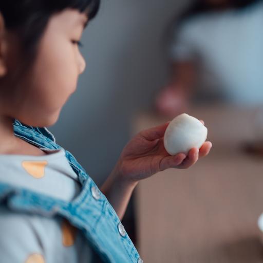 Blick über die Schulter eines Kindes, das ein angebissenes gekochtes Ei in der Hand anschaut.