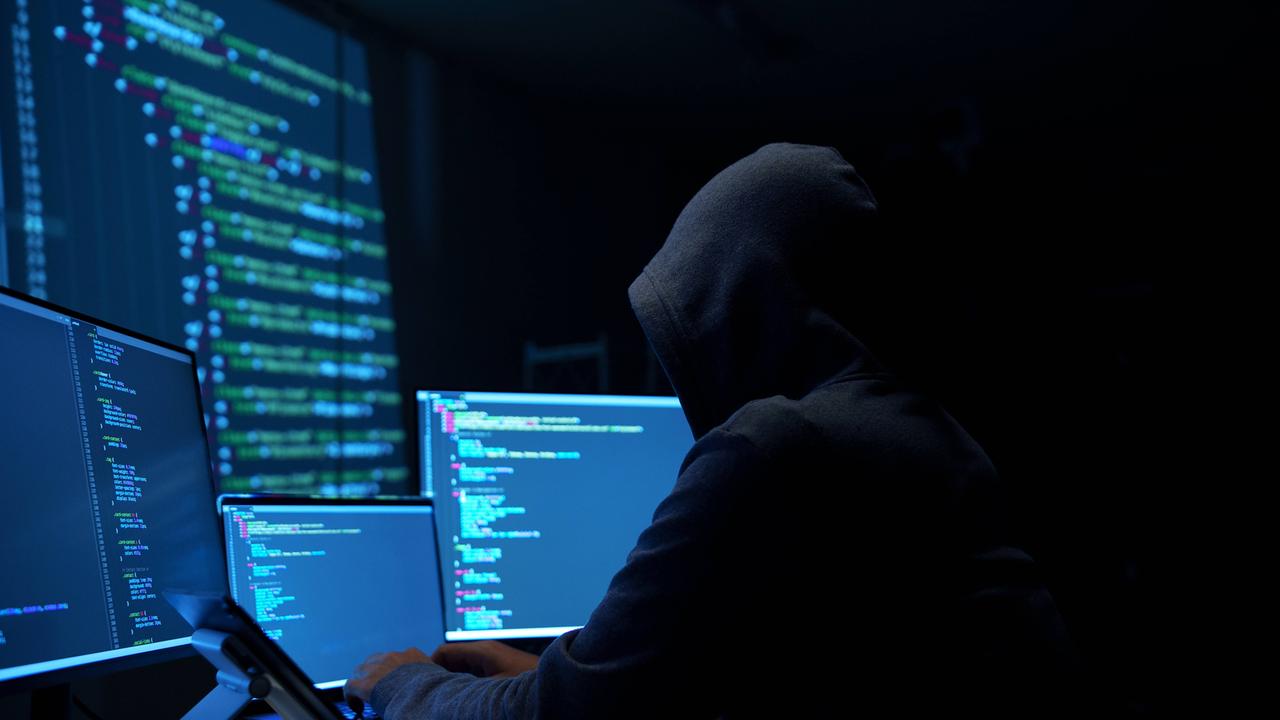 Ein Mann mit einem Kapuzen-Pulli sitzt vor mehreren Computer-Bildschirmen. Sein Gesicht ist nicht zu sehen.