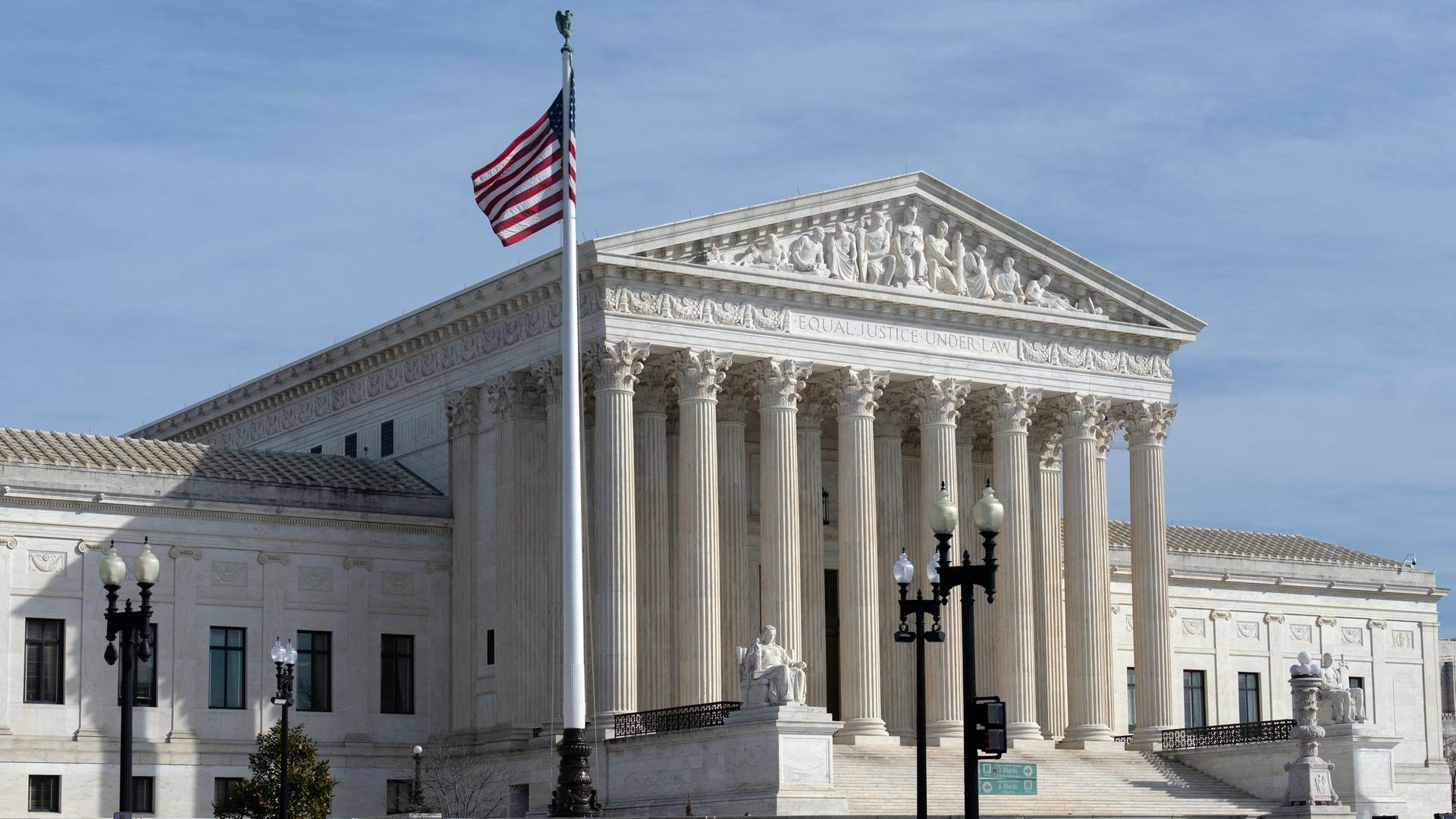 Außenansicht des U.S. Supreme Court: ein großes, weißes Gerichtsgebäude mit vielen Säulen und einer US-Flagge davor