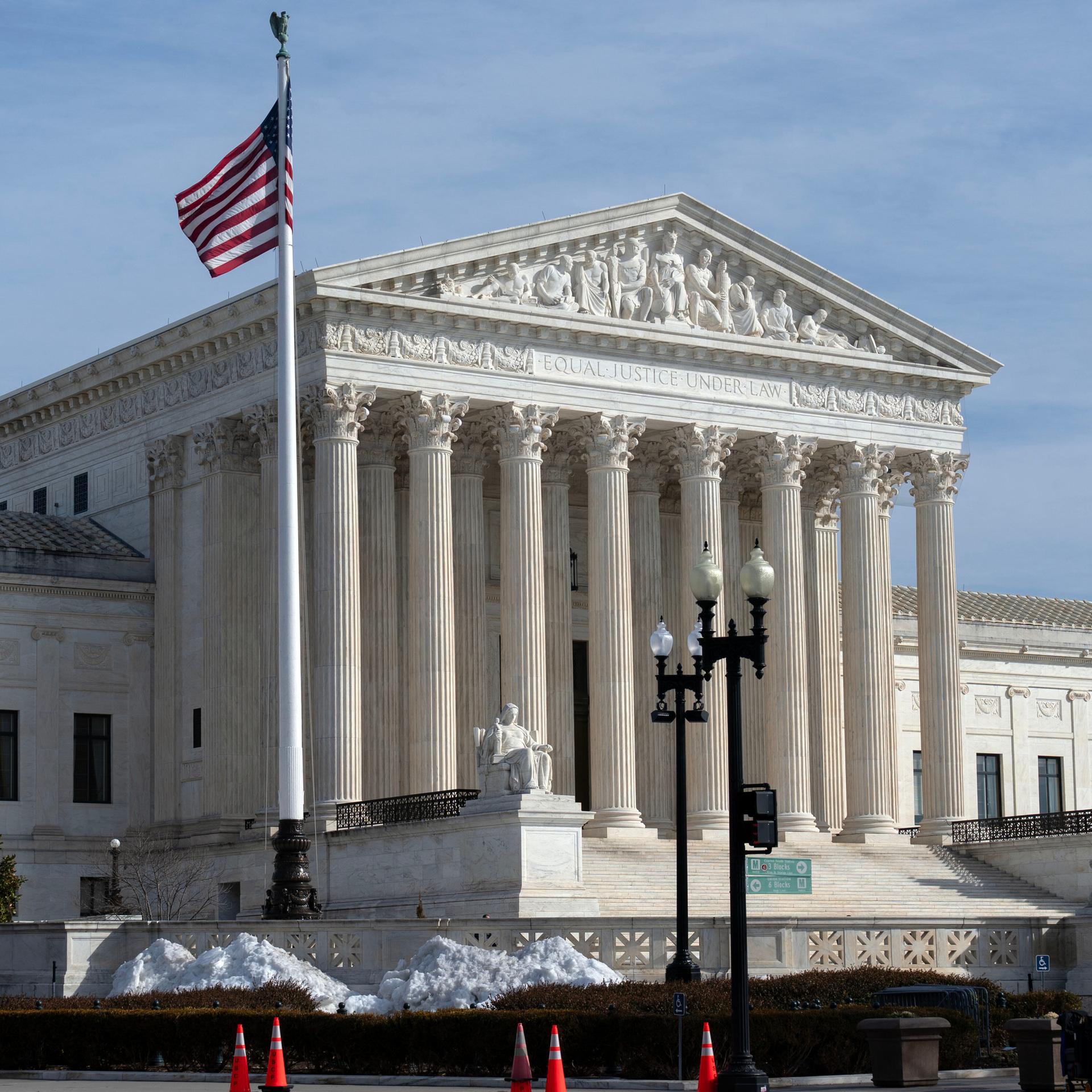 Außenansicht des U.S. Supreme Court: ein großes, weißes Gerichtsgebäude mit vielen Säulen und einer US-Flagge davor