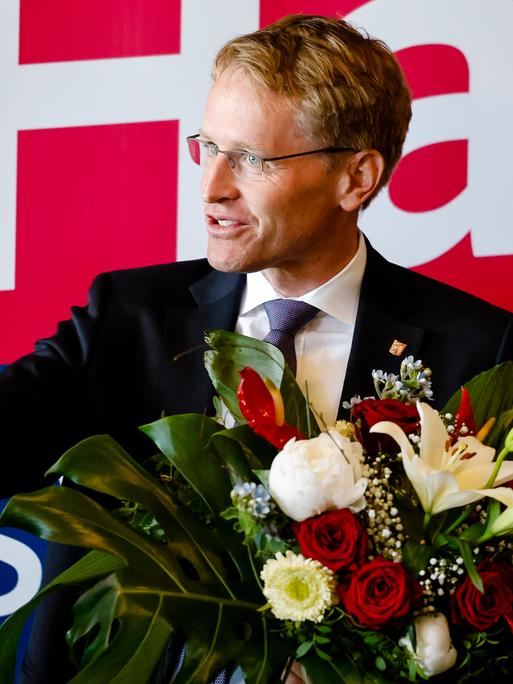 Ministerpräsident Daniel Günther hält einen Blumenstrauß und lächelt. Ministerpräsident Daniel Günther hält einen Blumenstrauß und lächelt.
