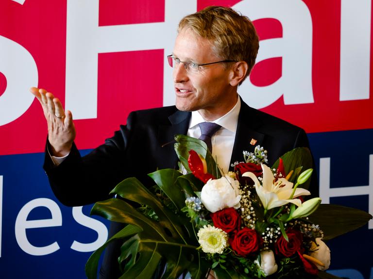 Ministerpräsident Daniel Günther hält einen Blumenstrauß und lächelt. Ministerpräsident Daniel Günther hält einen Blumenstrauß und lächelt.