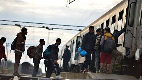 Flüchtlinge stehen auf Bahngleisen und besteigen einen Zug. Dabei werden sie von der Polizei begleitet.