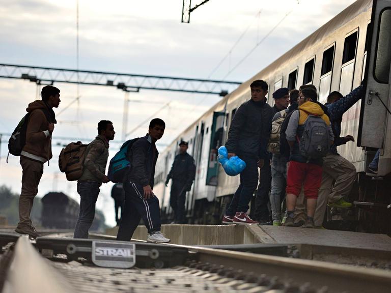 Flüchtlinge stehen auf Bahngleisen und besteigen einen Zug. Dabei werden sie von der Polizei begleitet.