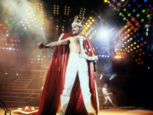 Queen-Frontmann Freddie Mercury steht in königlicher Robe und mit Krone auf dem Kopf auf der bunt beleuchteten Konzertbühne Queen-Frontmann Freddie Mercury steht in königlicher Robe und mit Krone auf dem Kopf auf der bunt beleuchteten Konzertbühne