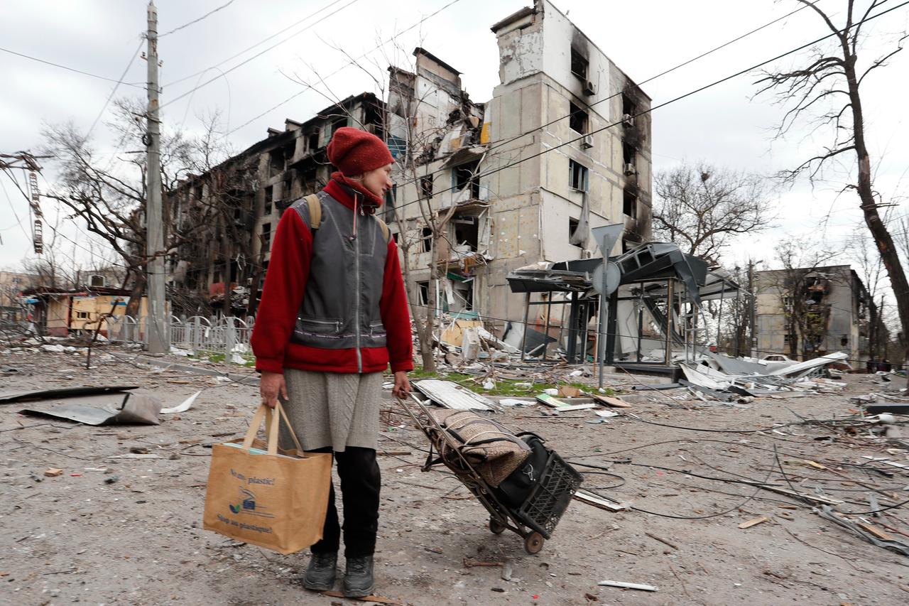 Ukraine, Mariupol: Eine Anwohnerin geht mit Gepäck an einem beschädigten Wohnhaus vorbei. Ukraine, Mariupol: Eine Anwohnerin geht mit Gepäck an einem beschädigten Wohnhaus vorbei.