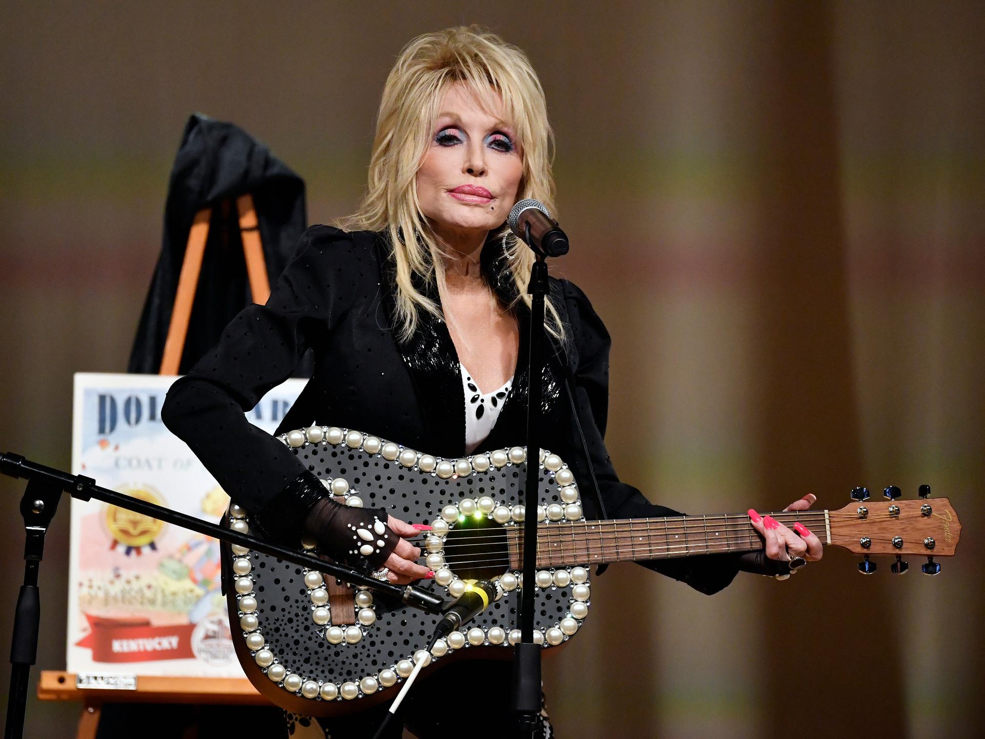 Dolly Parton steht mit einer Gitarre auf einer Bühne. 