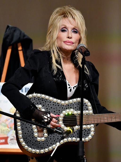 Dolly Parton steht mit einer Gitarre auf einer Bühne.