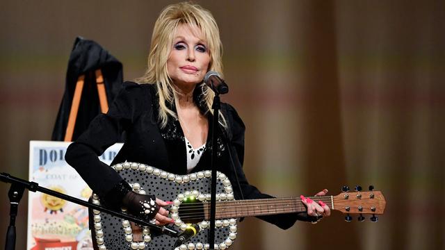 Dolly Parton steht mit einer Gitarre auf einer Bühne. 