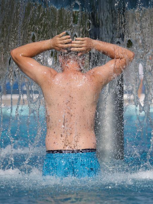 Ein Mann steht bei Temperaturen von über 30 Grad im Freibad unter einem Wasserpilz.