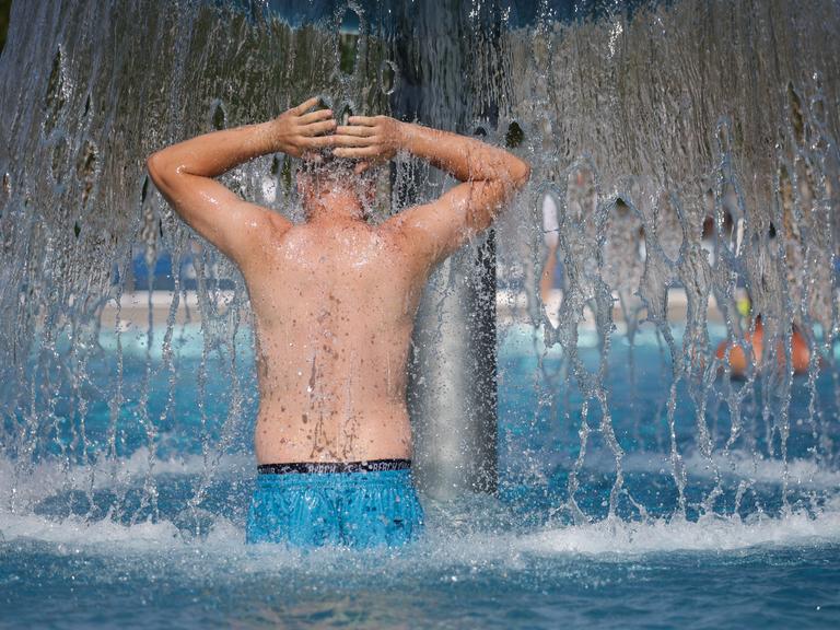 Ein Mann steht bei Temperaturen von über 30 Grad im Freibad unter einem Wasserpilz.