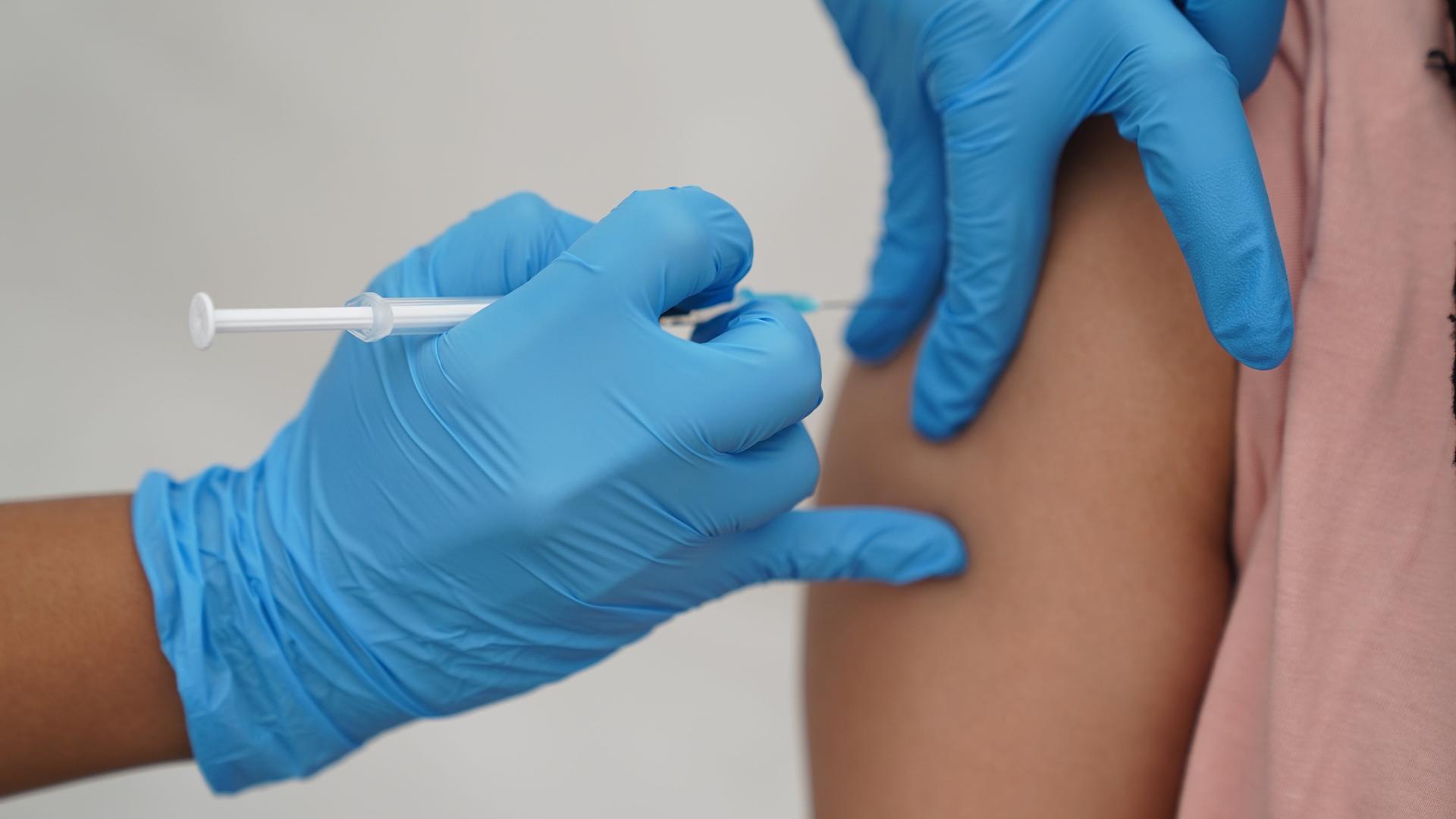 Zwei Hände mit blauen Handschuhen verabreichen eine Corona-Impfung 