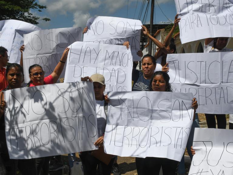 Menschen halten vor einem Gefängnis Plakate hoch. Darauf Aufschriften wie: "Gerechtigkeit" oder "Sie sind keine Terroristen". Menschen halten vor einem Gefängnis Plakate hoch. Darauf Aufschriften wie: "Gerechtigkeit" oder "Sie sind keine Terroristen".