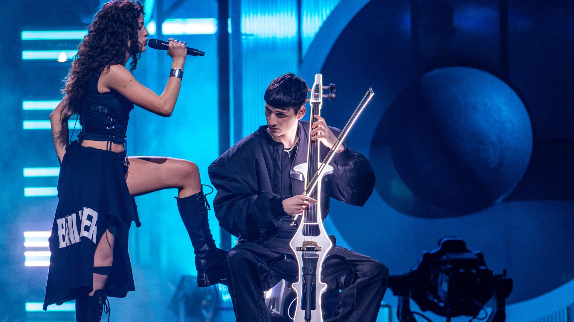 Das Duo Abor & Tynna während eines Auftritts. „Abor“ spielt Cello im Sitzen, während seine Schwester „Tynna“ stehend singt und ein Bein auf seinen Stuhl stellt. Das Duo Abor & Tynna während eines Auftritts. „Abor“ spielt Cello im Sitzen, während seine Schwester „Tynna“ stehend singt und ein Bein auf seinen Stuhl stellt.