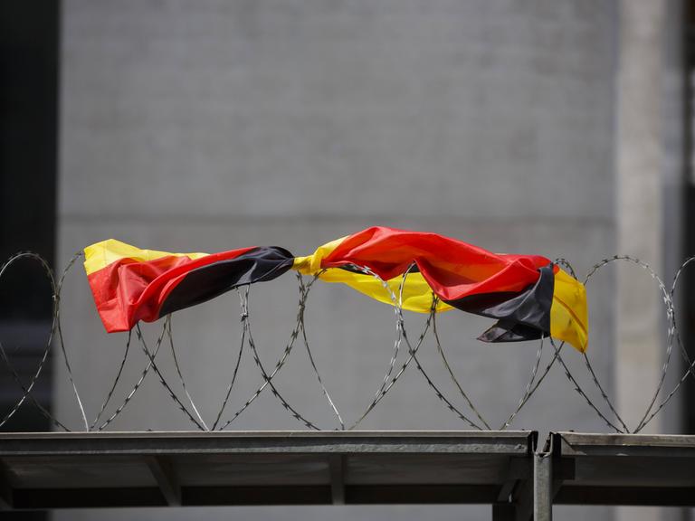 Eine Flagge der Bundesrepublik Deutschland liegt auf dem Stacheldrahtzaun einer Baustelle.