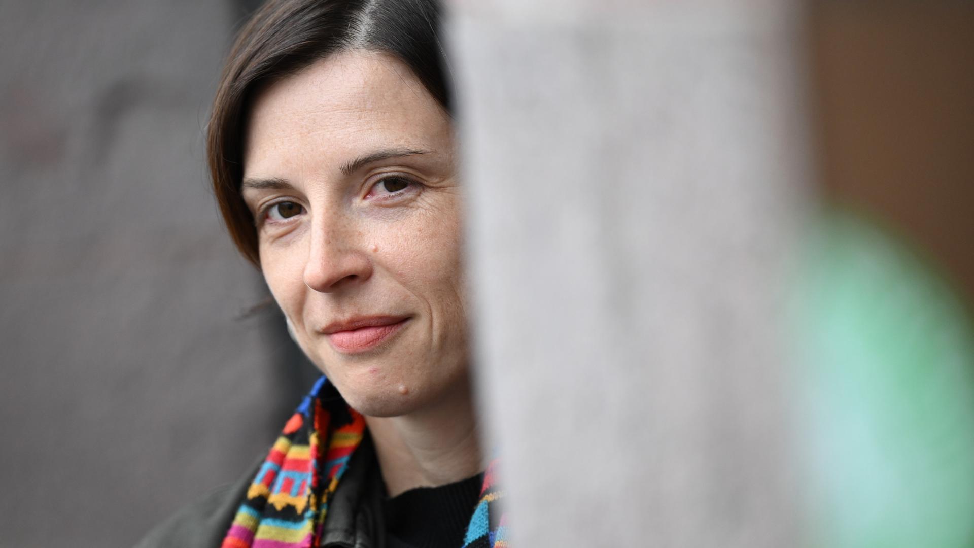 Dorothee Elmiger blickt um eine Ecke und trägt einen bunten Schal Dorothee Elmiger blickt um eine Ecke und trägt einen bunten Schal