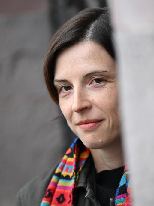 Dorothee Elmiger blickt um eine Ecke und trägt einen bunten Schal