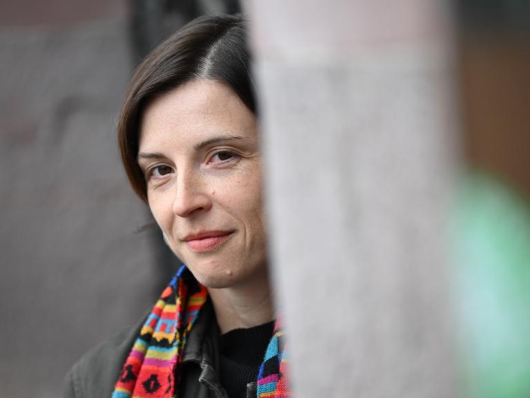 Dorothee Elmiger blickt um eine Ecke und trägt einen bunten Schal