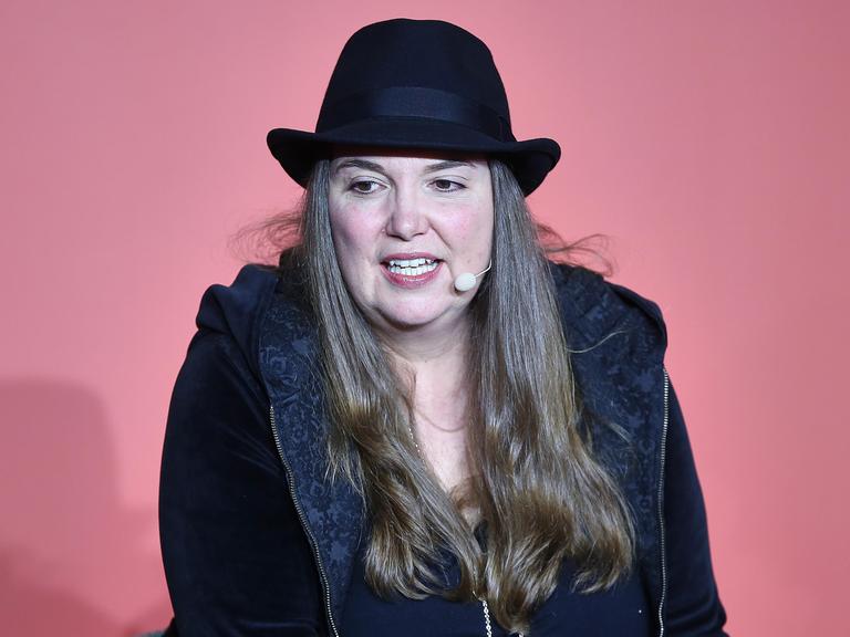 Tanya Stewner spricht bei der Frankfurter Buchmesse 2025 auf einer Bühne vor einem roten Hintergrund in ein Mikrofon. Sie trägt einen schwarzen Hut. Tanya Stewner spricht bei der Frankfurter Buchmesse 2025 auf einer Bühne vor einem roten Hintergrund in ein Mikrofon. Sie trägt einen schwarzen Hut.