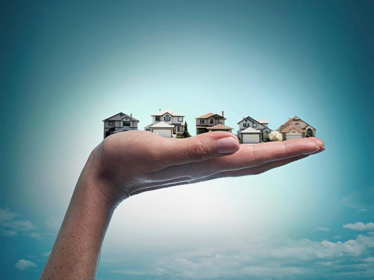 Eine Hand hält mehrere Häuser in den blauen Himmel.