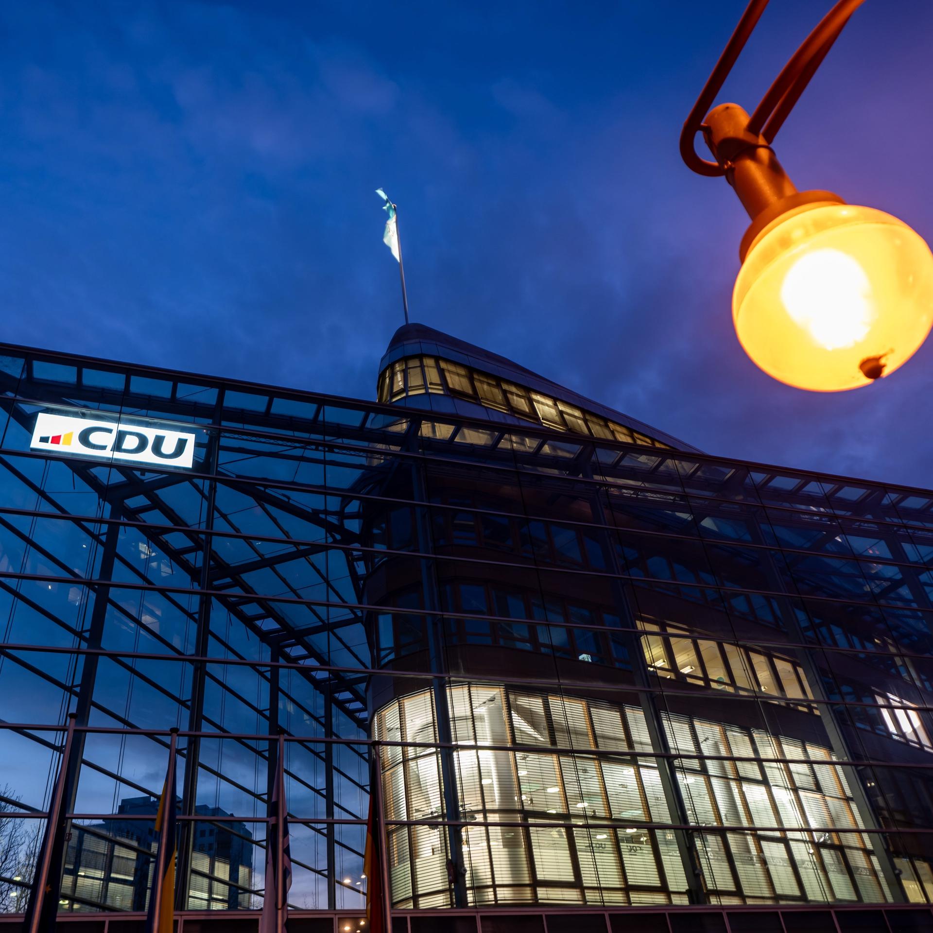 Blick von unten auf das Adenauer-Haus in der Abenddämmerung. In der oberen Bildhälfte im Vordergrund eine leuchtende Laterne. 