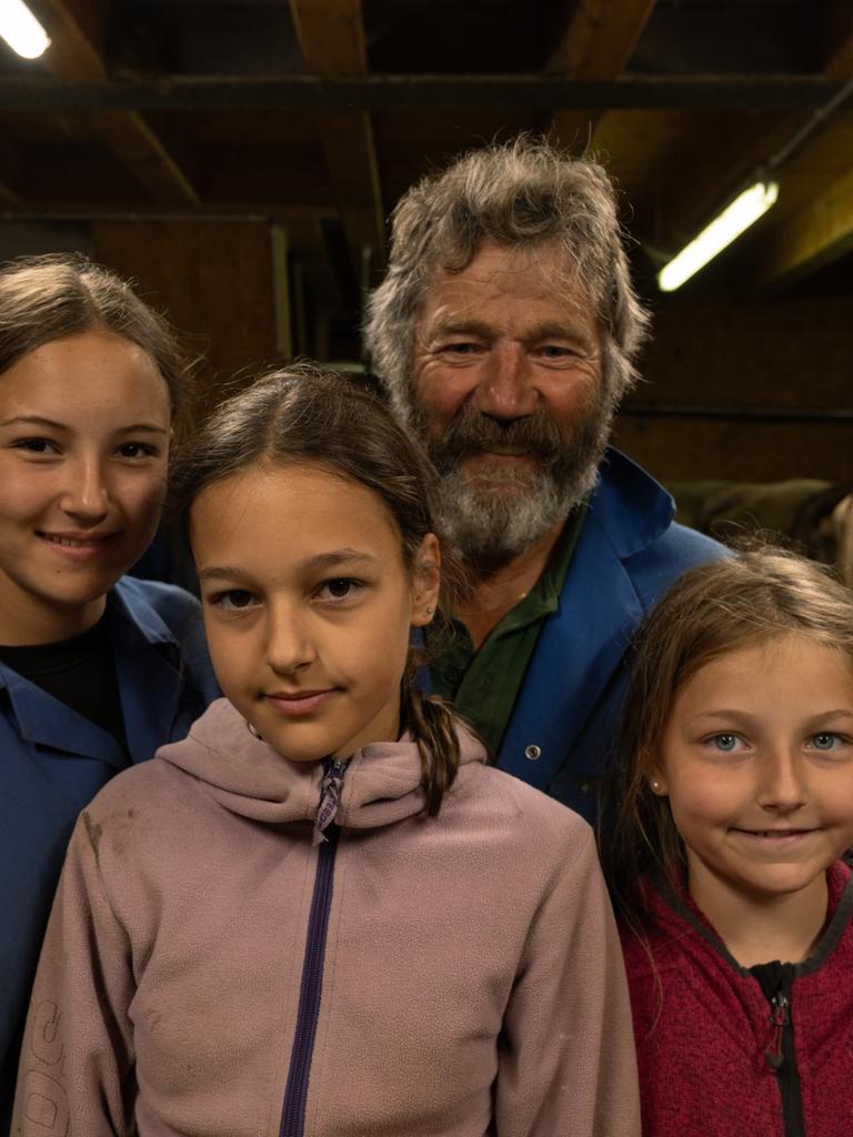 Hermann Bickel, ein älterer Herr in blauer Arbeitsjacke, und drei junge Mädchen lächeln in die Kamera. Im Hintergrund Kühe im Stall.