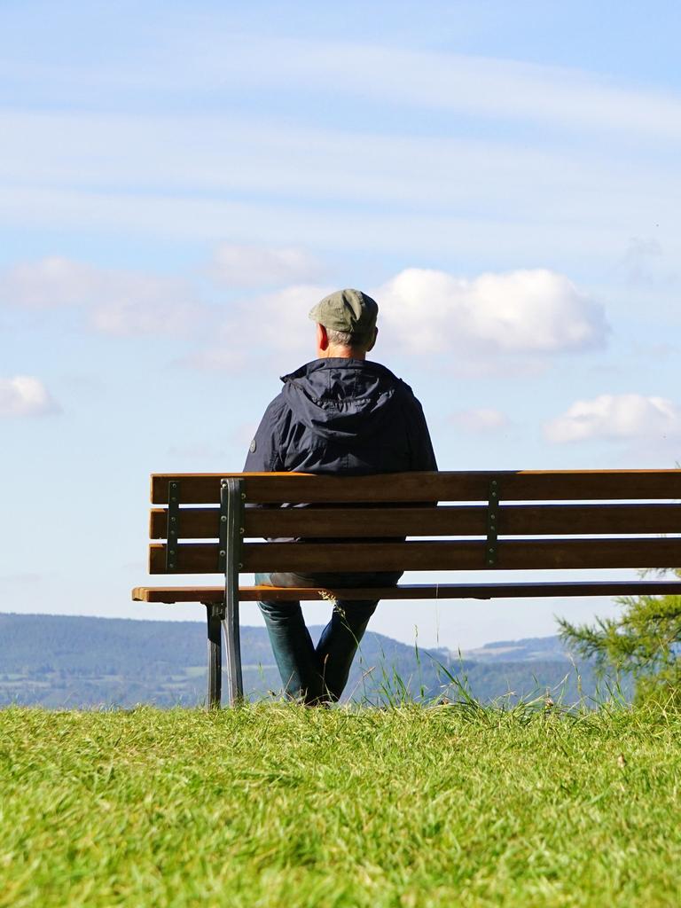 Ein älterer Herr sitzt mit dem Rücken zum Betrachter auf einer Parkbank mit Blick in die Ferne. Ein älterer Herr sitzt mit dem Rücken zum Betrachter auf einer Parkbank mit Blick in die Ferne.